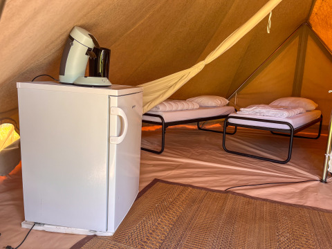 Interno di una tenda tipi al Camping Fuussekaul in Lussemburgo con due letti, frigorifero e macchina da caffè.