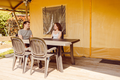 Two people sitting at a table outside a safari tent at Camping Liefrange in Luxembourg.