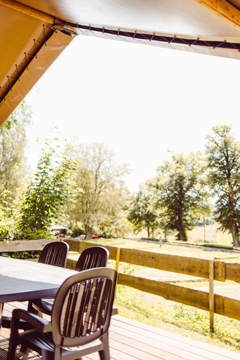 View from a safari tent terrace with black table and chairs at Camping Liefrange in Luxembourg, surrounded by nature.