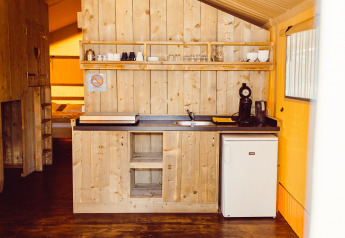 Angolo cottura in legno con macchina da caffè, frigo e scaffali in una tenda safari al Camping Liefrange.