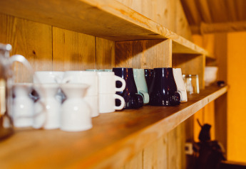 Cups and mugs on a wooden shelf inside the Camping Liefrange safaritent in Luxembourg with warm lighting.