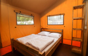 Intérieur d'une tente safari au Camping Liefrange au Luxembourg avec lit double et étagère en bois.