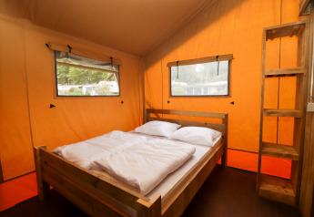 Interior of a safari tent at Camping Liefrange in Luxembourg with a double bed and wooden shelves.