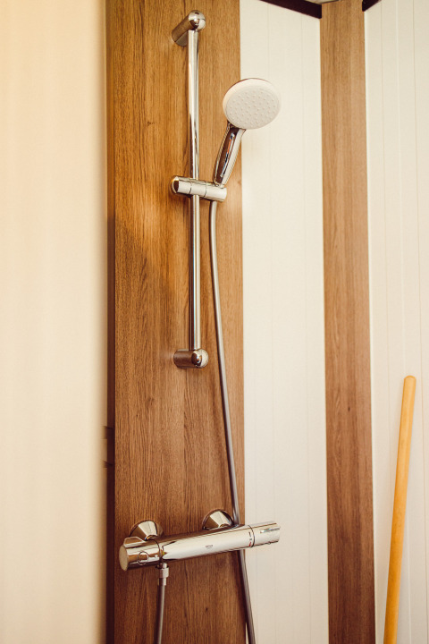 Modern shower with chrome head and wood panel in a safari tent at Camping Liefrange, Luxembourg.
