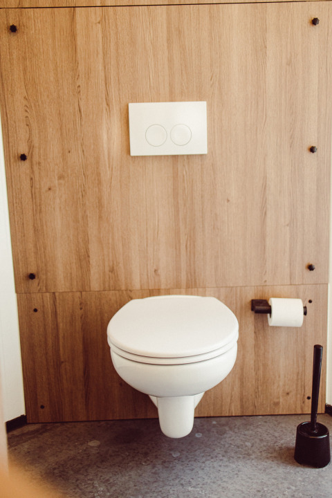 Toilette sospesa moderna con parete in legno, carta igienica e scopino in una tenda safari in Lussemburgo.