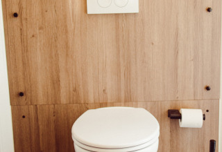Modern wall-mounted toilet with wood panel wall, toilet paper and brush in a safari tent in Luxembourg.