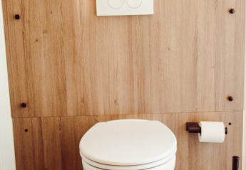 Modern hangtoilet met houten wand, toiletrol en borstel in een safaritent op Camping Liefrange Luxemburg.