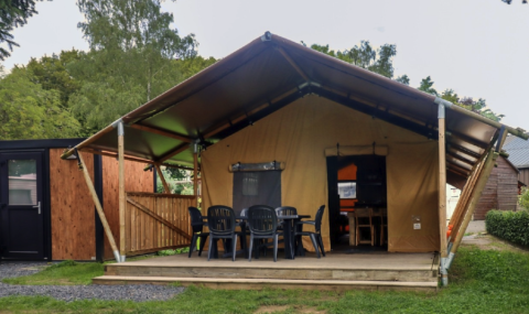 Safari tent at Camping Liefrange with front porch, plastic chairs, and surrounded by lush green nature.