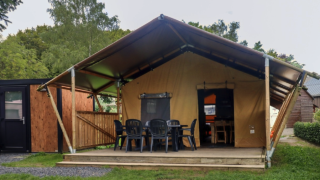 Tenda safari al Camping Liefrange con veranda anteriore, sedie nere e circondata dalla natura verde.