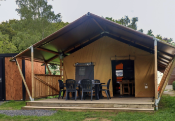Safari tent at Camping Liefrange with front porch, plastic chairs, and surrounded by lush green nature.