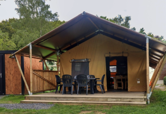 Tente safari au Camping Liefrange avec terrasse couverte, chaises noires et végétation environnante.