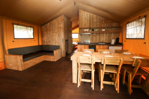 Intérieur d'une tente safari au Camping Liefrange au Luxembourg avec meubles en bois, table et cuisine.