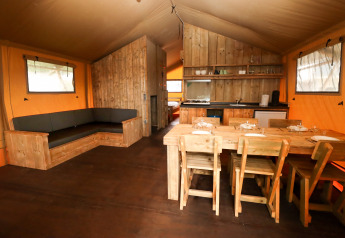 Safari tent interior at Camping Liefrange, Luxembourg with wooden furniture, dining table, and kitchen.