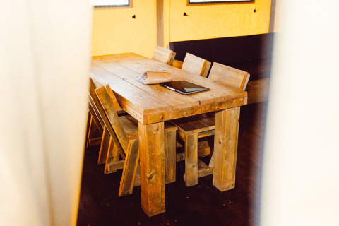 Wooden table and chairs inside a safari tent at Camping Liefrange in Luxembourg, with a notebook on the table.