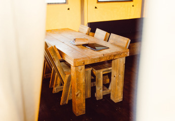 Houten tafel en stoelen in een safaritent bij Camping Liefrange in Luxemburg, met notitieboek op tafel.