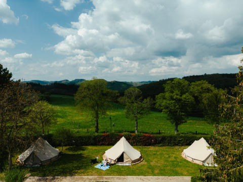 Tre tende tipi nel Camping Liefrange in Lussemburgo, circondate da prati verdi e alberi sotto un cielo nuvoloso.