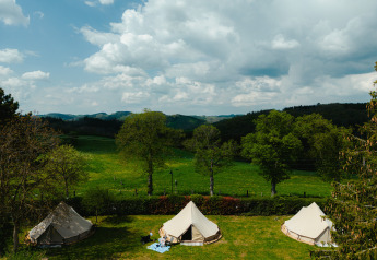 Three tipi tents at Camping Liefrange in Luxembourg, set on green fields with trees and a cloudy sky above.