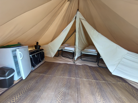 Intérieur du tipi Camping Liefrange avec lits, réfrigérateur et cuisinière au Camping Liefrange au Luxembourg.