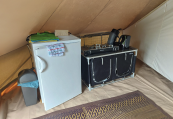 Angolo cucina in una tenda tipi con frigorifero, fornello, bollitore e tappeto al Camping Liefrange.