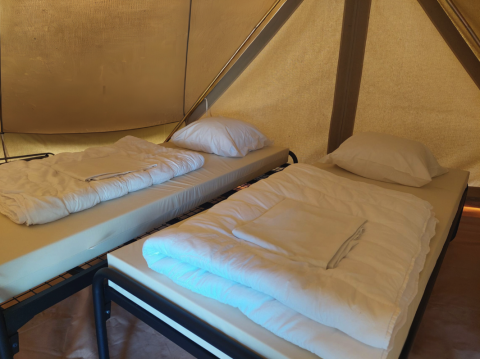 Zwei Einzelbetten mit weißen Decken und Kissen in einem Tipi-Zelt auf Camping Liefrange, Luxemburg.