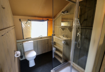Bathroom in a safari tent featuring a toilet, shower, and sink at Camping Liefrange in Luxembourg.