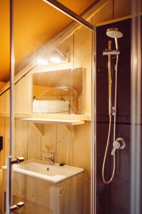 Bathroom with shower, sink, and mirror inside a safari tent lodge at Camping Liefrange in Luxembourg.