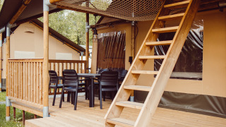 Safari tent with wooden deck, patio chairs, dining table, and loft ladder at Camping Liefrange - Ranger Lodge.