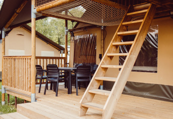 Safari tent with wooden deck, patio chairs, dining table, and loft ladder at Camping Liefrange - Ranger Lodge.