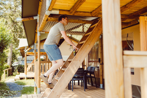 Man climbs wooden stairs to an upper level of a safari tent lodge at Camping Liefrange in Luxembourg.