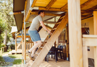 Uomo sale una scala di legno verso il livello superiore di una tenda safari al Camping Liefrange in Lussemburgo.