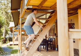 Uomo sale una scala di legno verso il livello superiore di una tenda safari al Camping Liefrange in Lussemburgo.