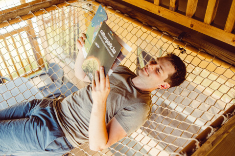 Man relaxing on a net hammock reading a magazine inside a safari tent at Camping Liefrange, Luxembourg.