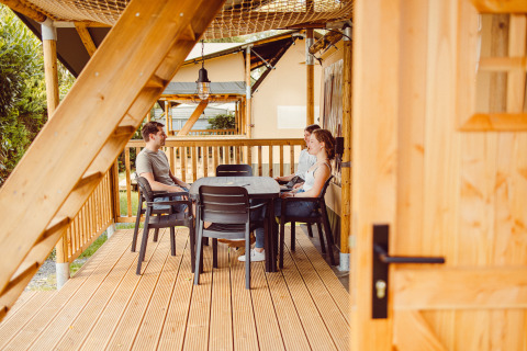 Tre persone che chiacchierano a un tavolo sulla terrazza di una tenda safari al Camping Liefrange.