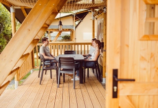 Tre persone che chiacchierano a un tavolo sulla terrazza di una tenda safari al Camping Liefrange.