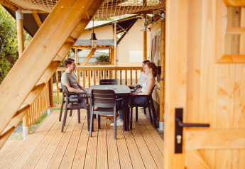Tre persone che chiacchierano a un tavolo sulla terrazza di una tenda safari al Camping Liefrange.