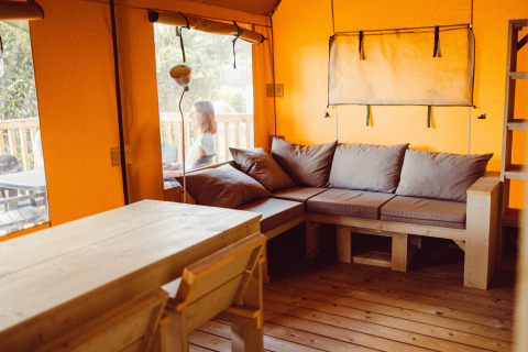 Cozy safari tent interior at Camping Liefrange, Ranger Lodge, with wood furniture and a person outside.