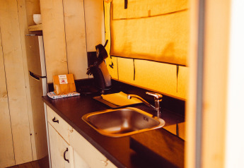 Kitchen area in a safari tent with sink, coffee maker, and fridge at Camping Liefrange, Ranger Lodge.