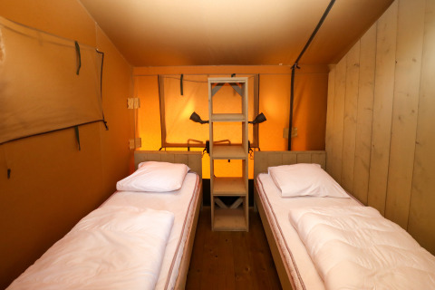 Interior of a safari tent with two single beds and a wooden shelf at Camping Liefrange, Luxembourg.