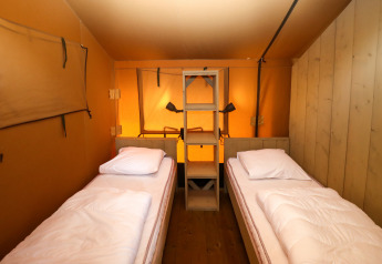 Interno di una tenda safari con due letti singoli e scaffale in legno al Camping Liefrange, Lussemburgo.