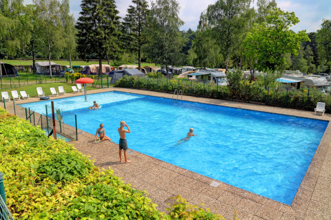 Piscina all'aperto con bambini, lettini prendisole e camper sullo sfondo ad Auf Kengert, Diekirch, Lussemburgo.