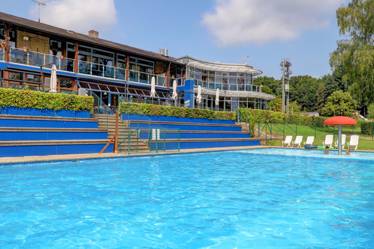 Udendørs swimmingpool ved en feriepark i Diekirch, Luxembourg, med solstole og moderne bygninger.