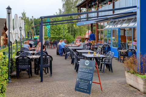 Outdoor restaurant terrace at Auf Kengert holiday park, Diekirch, Luxembourg, with guests dining at tables.