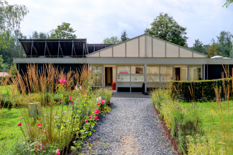 Ein blumenumgebener Weg führt zu einem modernen Gebäude im Ferienpark Auf Kengert in Diekirch, Luxemburg.