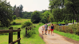 Family walking on a scenic path at Auf Kengert holiday park, surrounded by greenery in Diekirch, Luxembourg.