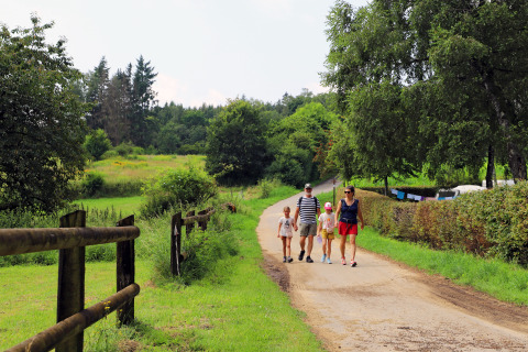 Familie på gåtur langs sti i frodigt landskab ved Auf Kengert feriepark, Diekirch, Luxembourg.