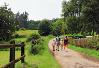 Family walking on a scenic path at Auf Kengert holiday park, surrounded by greenery in Diekirch, Luxembourg.