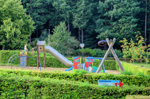 Aire de jeux avec toboggan et balançoires au parc de vacances Auf Kengert à Diekirch, Luxembourg, entouré de forêt.