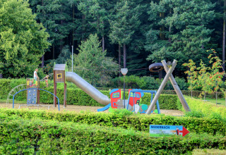 Legeplads omgivet af hæk og skov ved Auf Kengert feriepark i Diekirch, Luxembourg med gynger og rutsjebane.