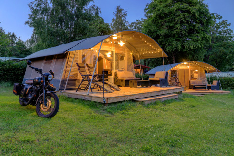 Glamping telte med terrasse, lys og motorcykel ved Auf Kengert feriepark, Diekirch, Luxembourg om aftenen.