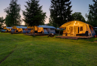 Aftenbillede af oplyste glamping telte og terrasseområder på Auf Kengert feriepark i Diekirch, Luxembourg.